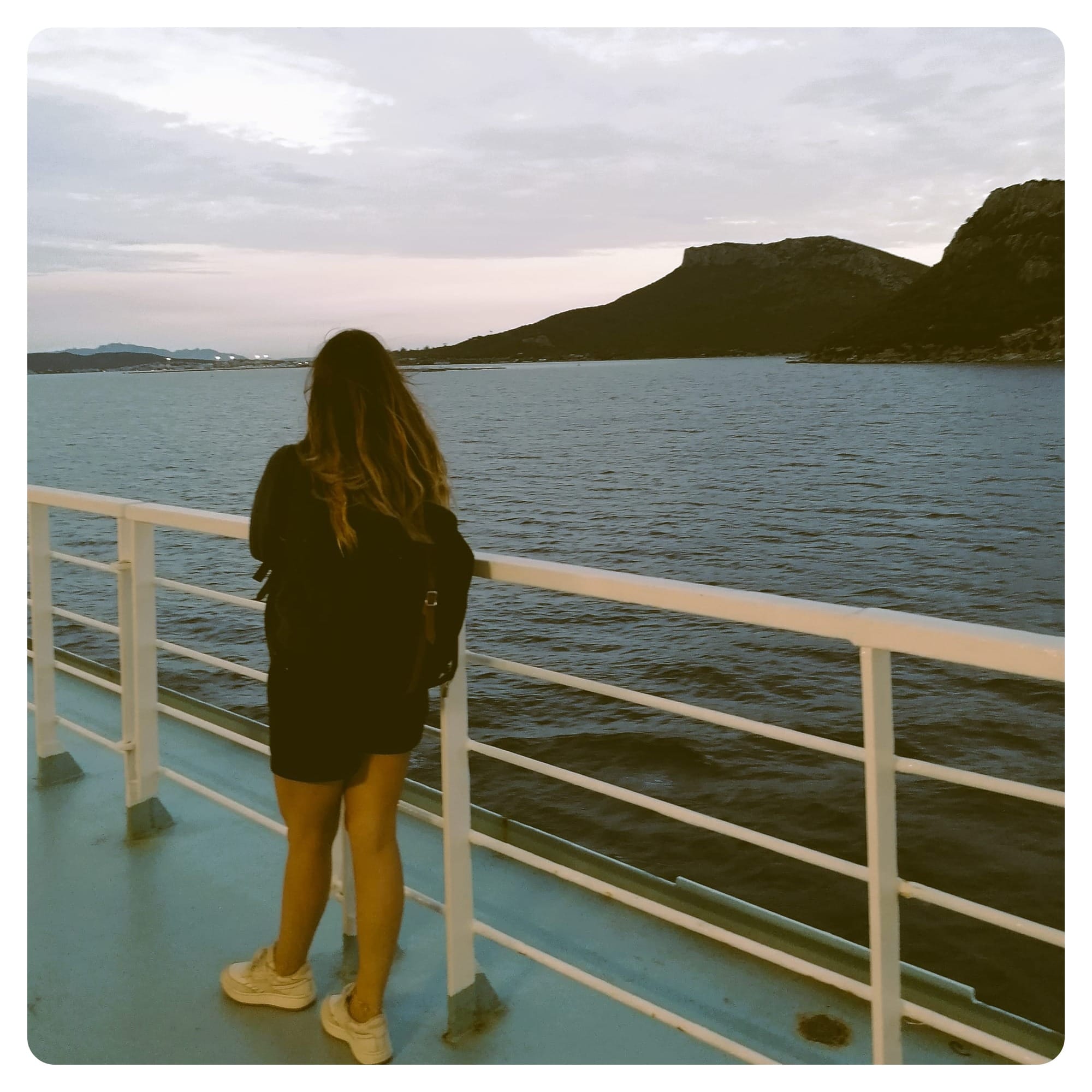 vanlavita woman stood on deck of a ferry overlooking the coastline of Sardinia