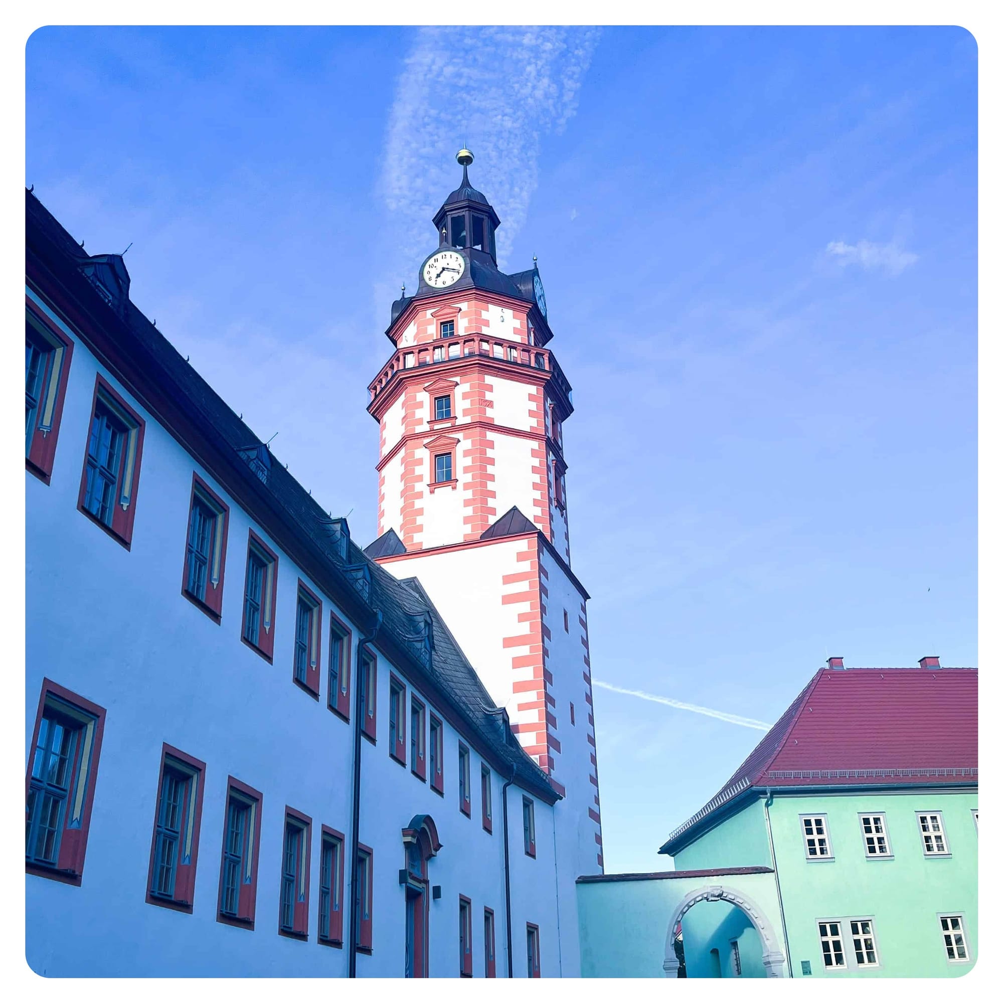 white clock tower next to building with green facade and red tiled roof in Ohrdruf, Germany