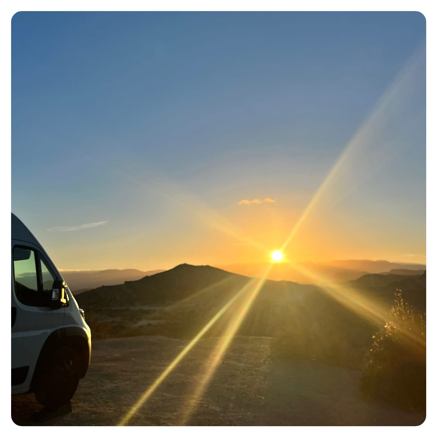 vanlife vanlavita white van overlooking the sun setting behind desert mountain