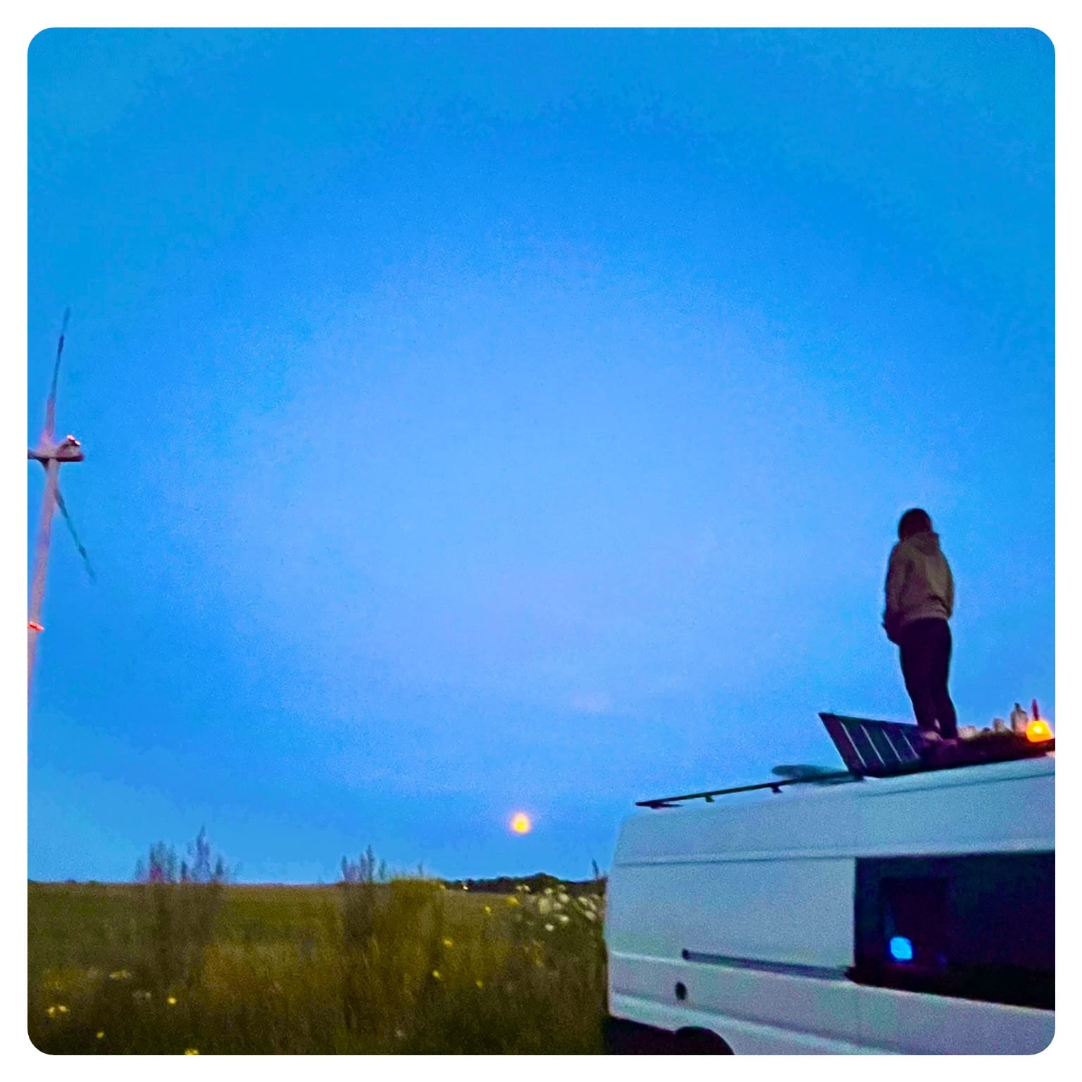 vanlife vanlavita woman stood on roof deck of a white van, looking at the moon
