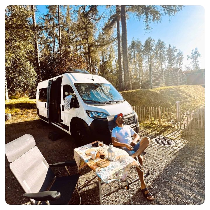 Van life man in sunshine at outdoor campsite next to his camper van 