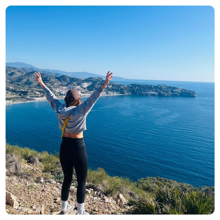 vanlavita woman standing on cliff edge overlooking a blue sea 
