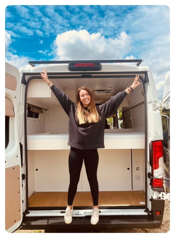 vanlife vanlavita woman stood next to a white panel van with arms extended 