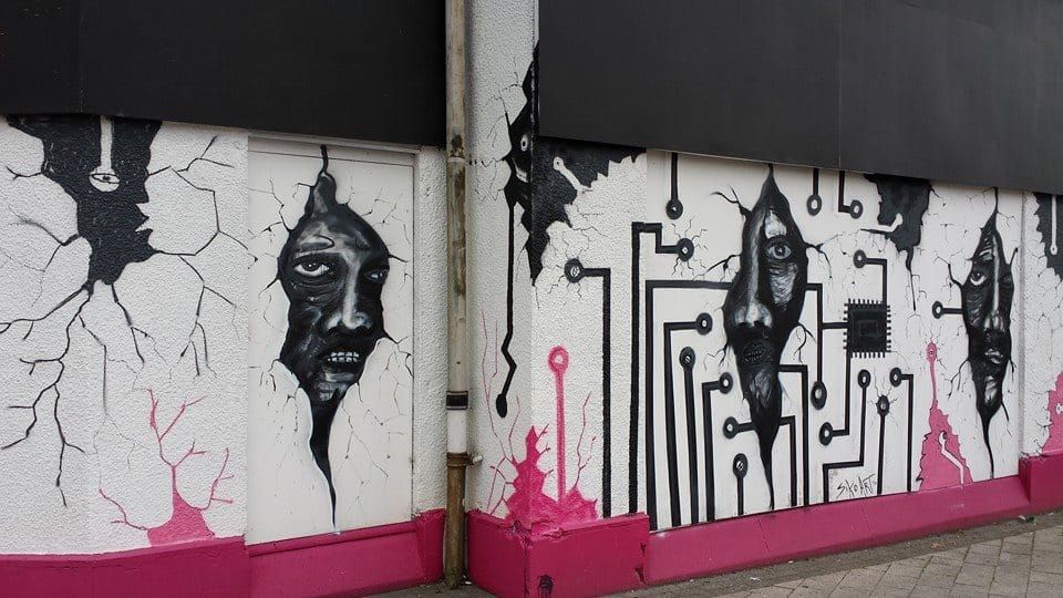 Artwork on the outer walls of the organisation's base of operations, featuring faces peering through what looks like circuitboard in the wall.
