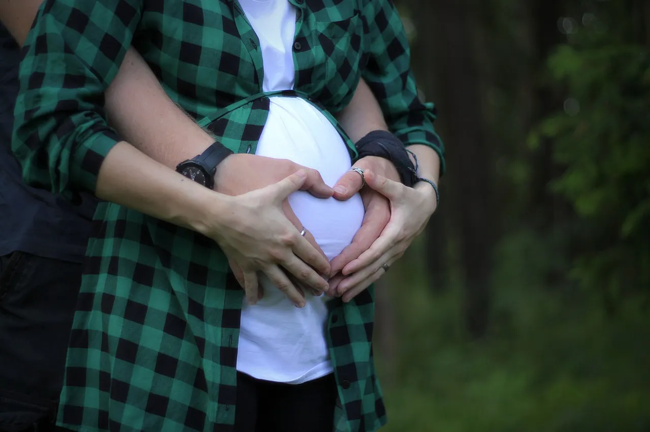 Pareja haciendo corazón con las manos sobre barriga de embarazada