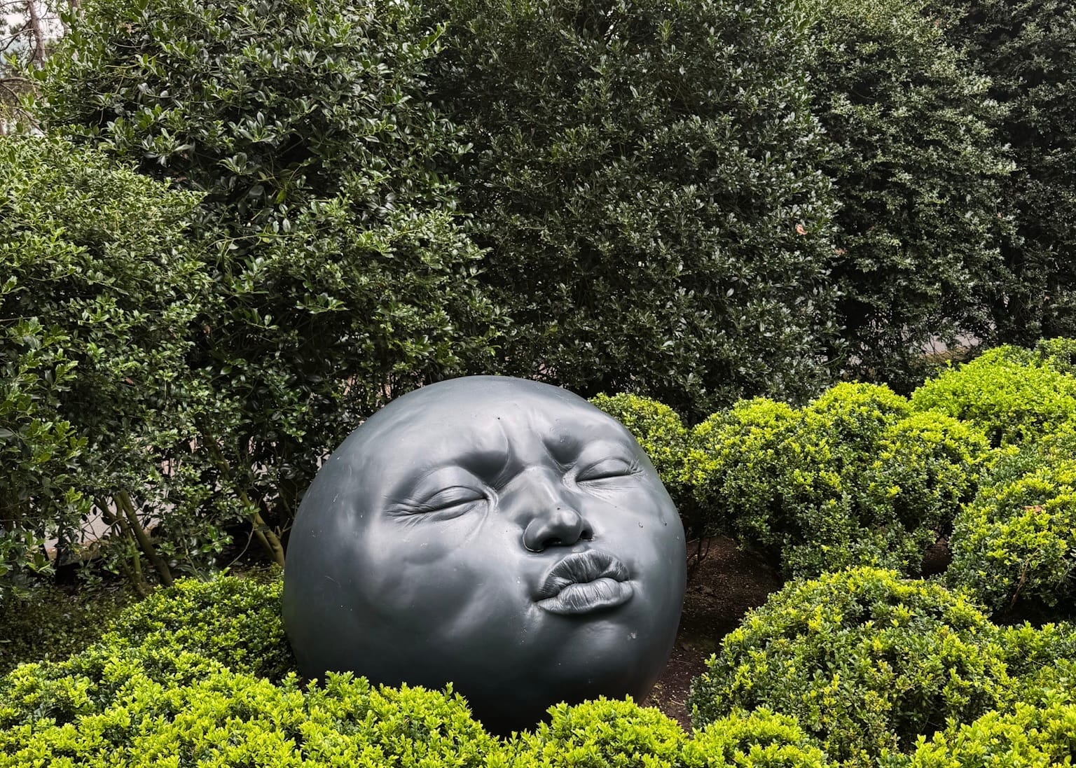 A contemporary sculpture of a serene face nestled among sculpted hedges at Les Jardins d'Étretat in Normandy, France.