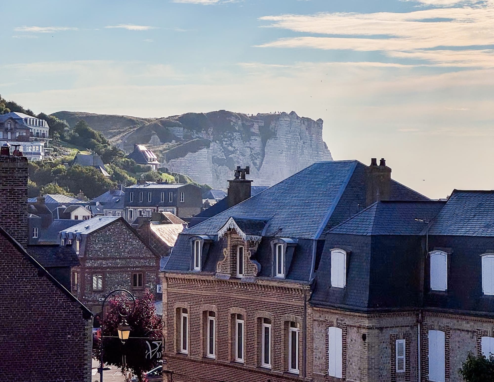 View over the rooftops of Étretat, France, with the town's iconic white chalk cliffs rising in the background.
