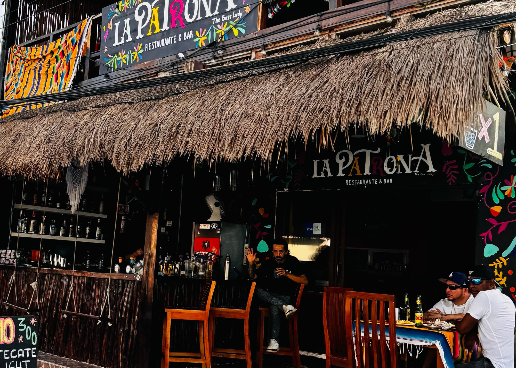 Colorful exterior of La Patrona Restaurant & Bar in Isla Mujeres, Mexico, featuring a traditional palapa roof, rooftop seating, vibrant Mexican décor, and open-air dining
