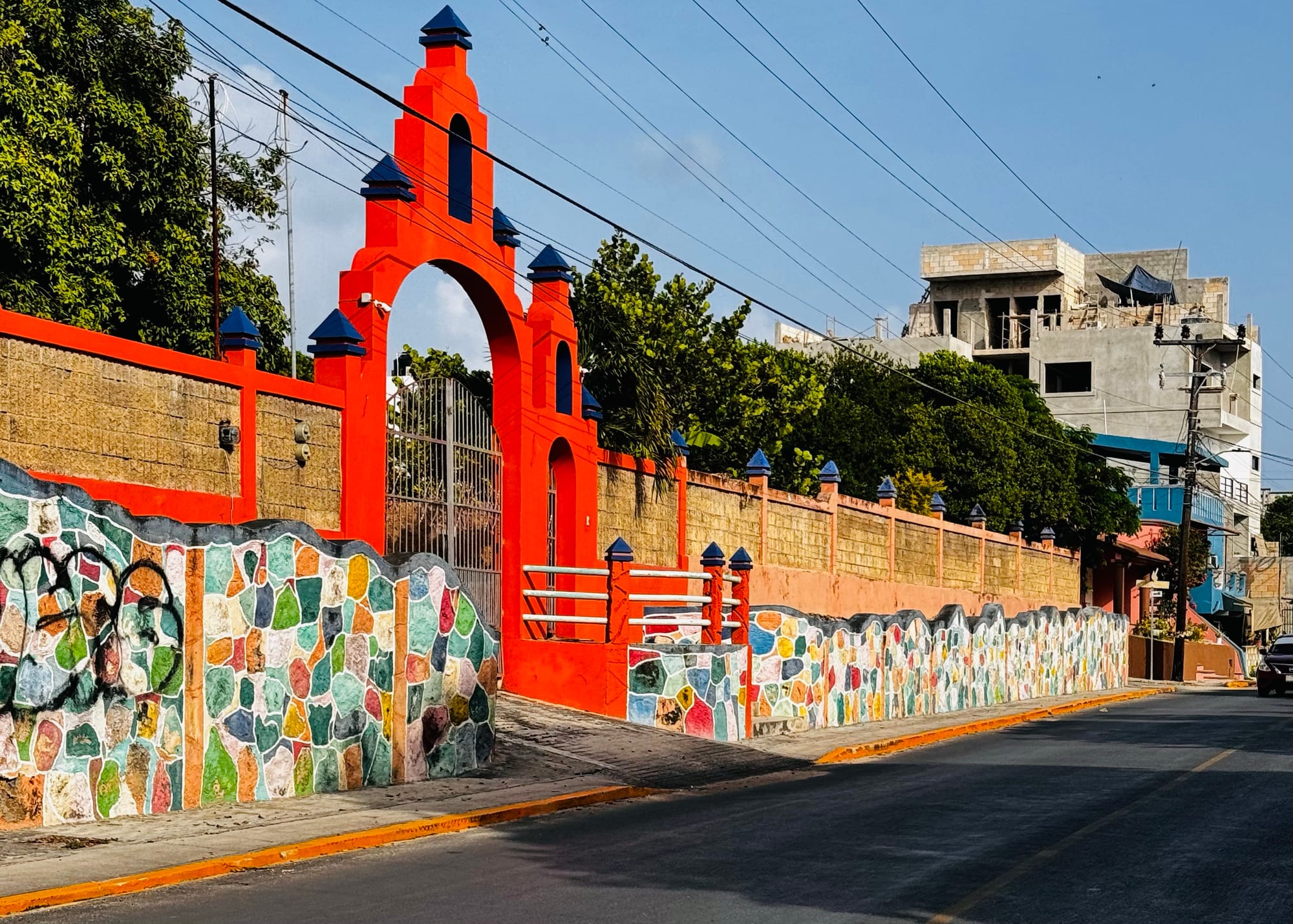 A vibrant coral-colored entrance framed by a colorful mosaic stone wall along a quiet street in Isla Mujeres, Mexico