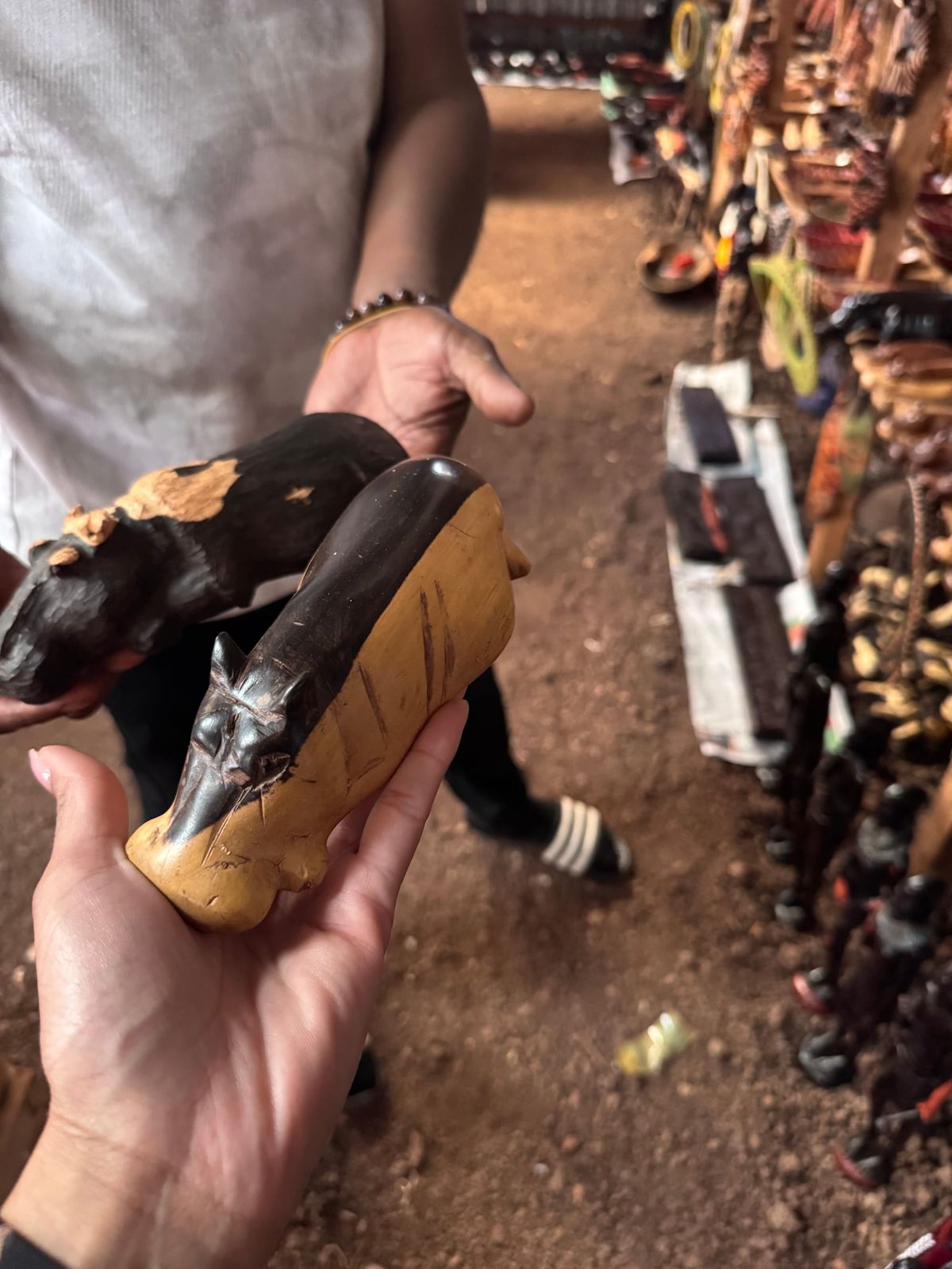 A hand holds a handcrafted wooden carving at an artisan market in Tanzania while another carving is presented in the background.