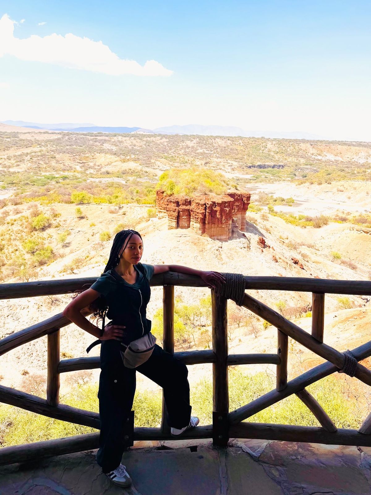 Lynai standing at the Olduvai Gorge overlook in Tanzania, with the rugged archaeological landscape stretching into the distance behind her.