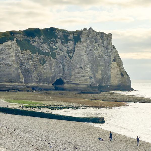 The famous white chalk cliffs of Étretat rise above the pebble beach along the Normandy coast in France.