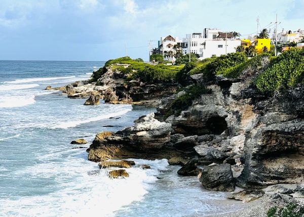 Waves crash against limestone cliffs along the eastern coast of Isla Mujeres with homes overlooking the Caribbean Sea under dramatic skies