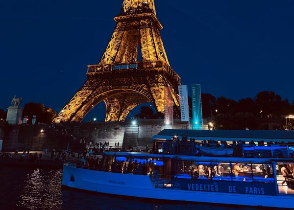 The Eiffel Tower illuminated at night as a sightseeing boat cruises along the Seine River in Paris, France.
