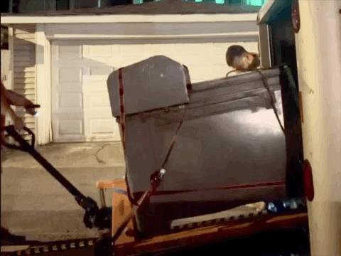A gif of a press sliding out of a truck at alarming speed while the two men moving it jump back