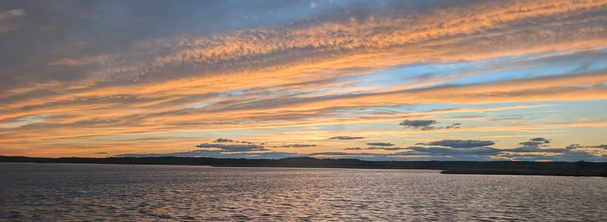 The evening sky with pink clouds over a body of water seen from inside an Amtrak train.