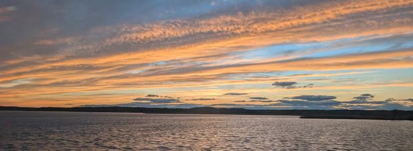 The evening sky with pink clouds over a body of water seen from inside an Amtrak train.