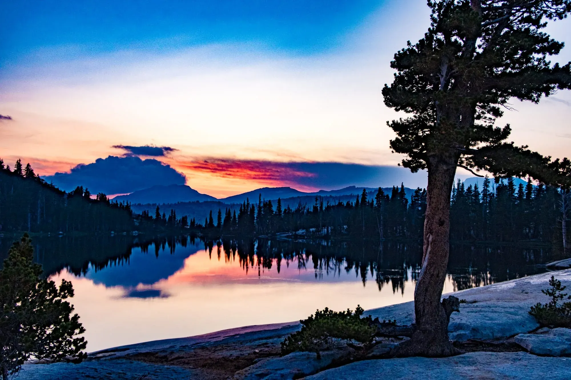 Alpine lake reflecting sunset colors and mountain silhouettes in Yosemite backcountry with granite shore