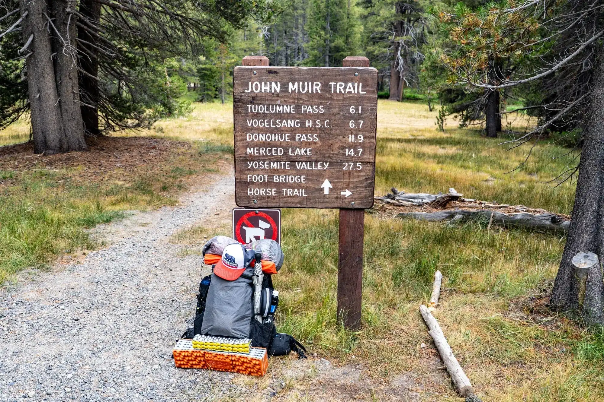 Backpacking gear and packs at John Muir Trail trailhead sign showing distances to wilderness destinations