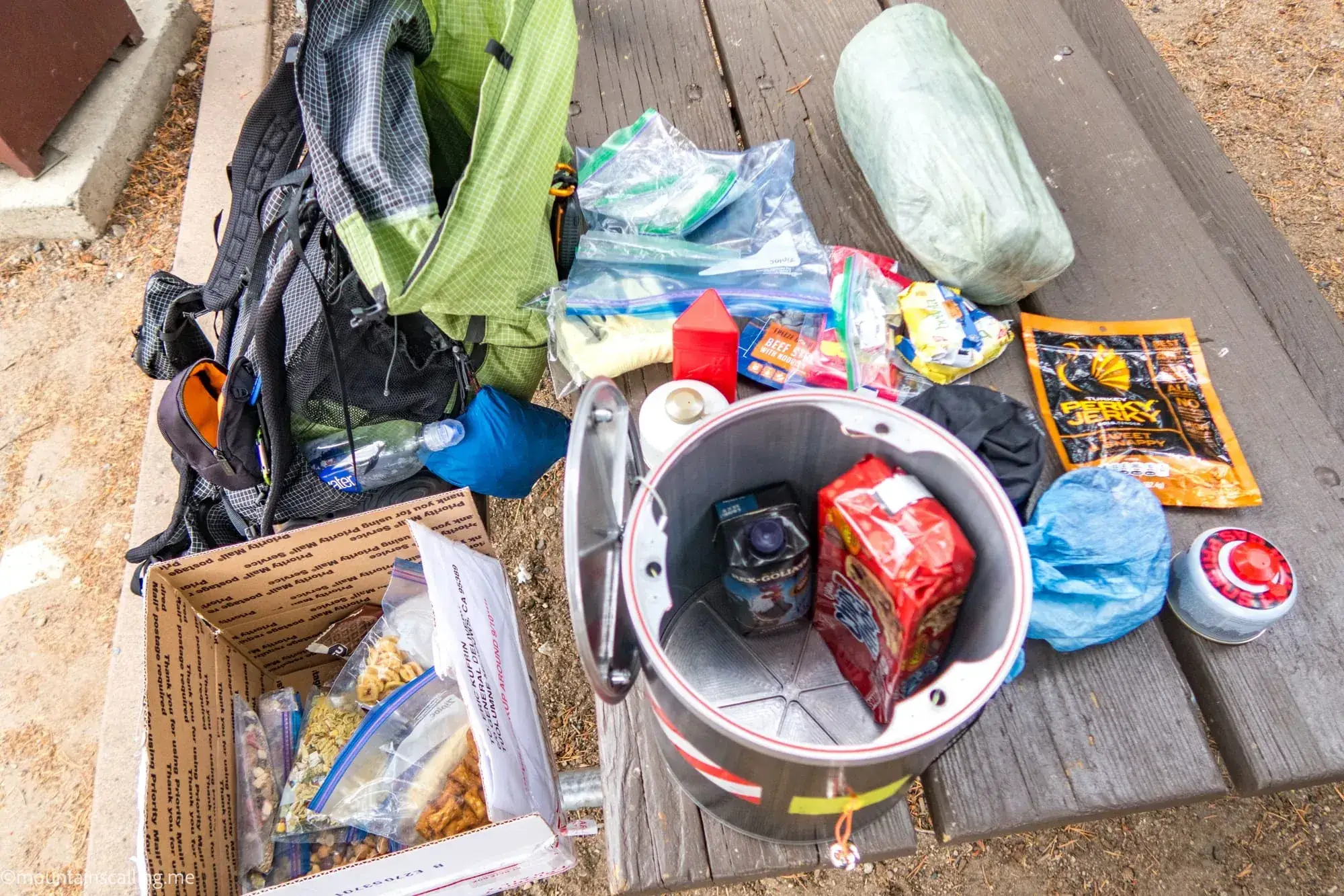 Backpacking gear and food spread out during resupply including bear canister, backpack, and food packages