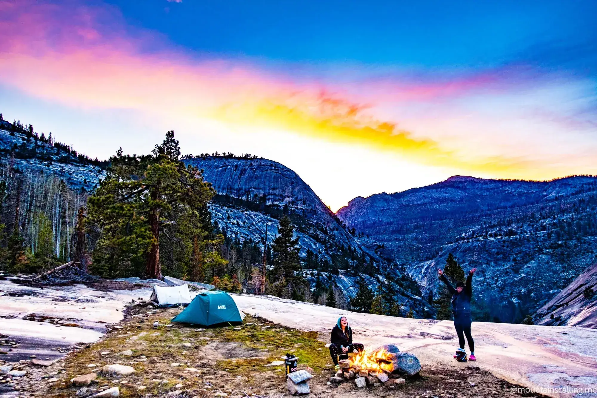 Backpackers around campfire at sunset with granite domes during guided Yosemite wilderness backpacking trip