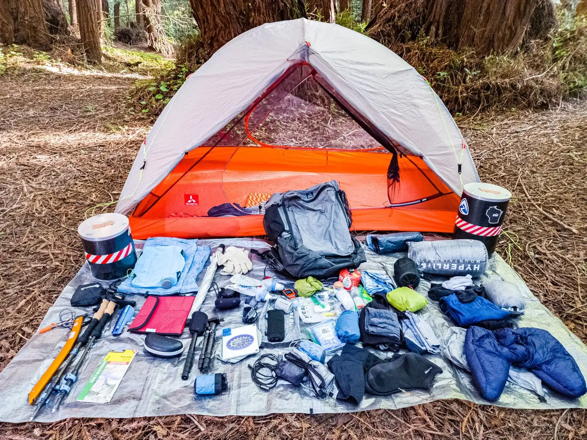 Backpacking gear spread out on tarp in front of tent at Yosemite wilderness campsite showing essential items for guided trips