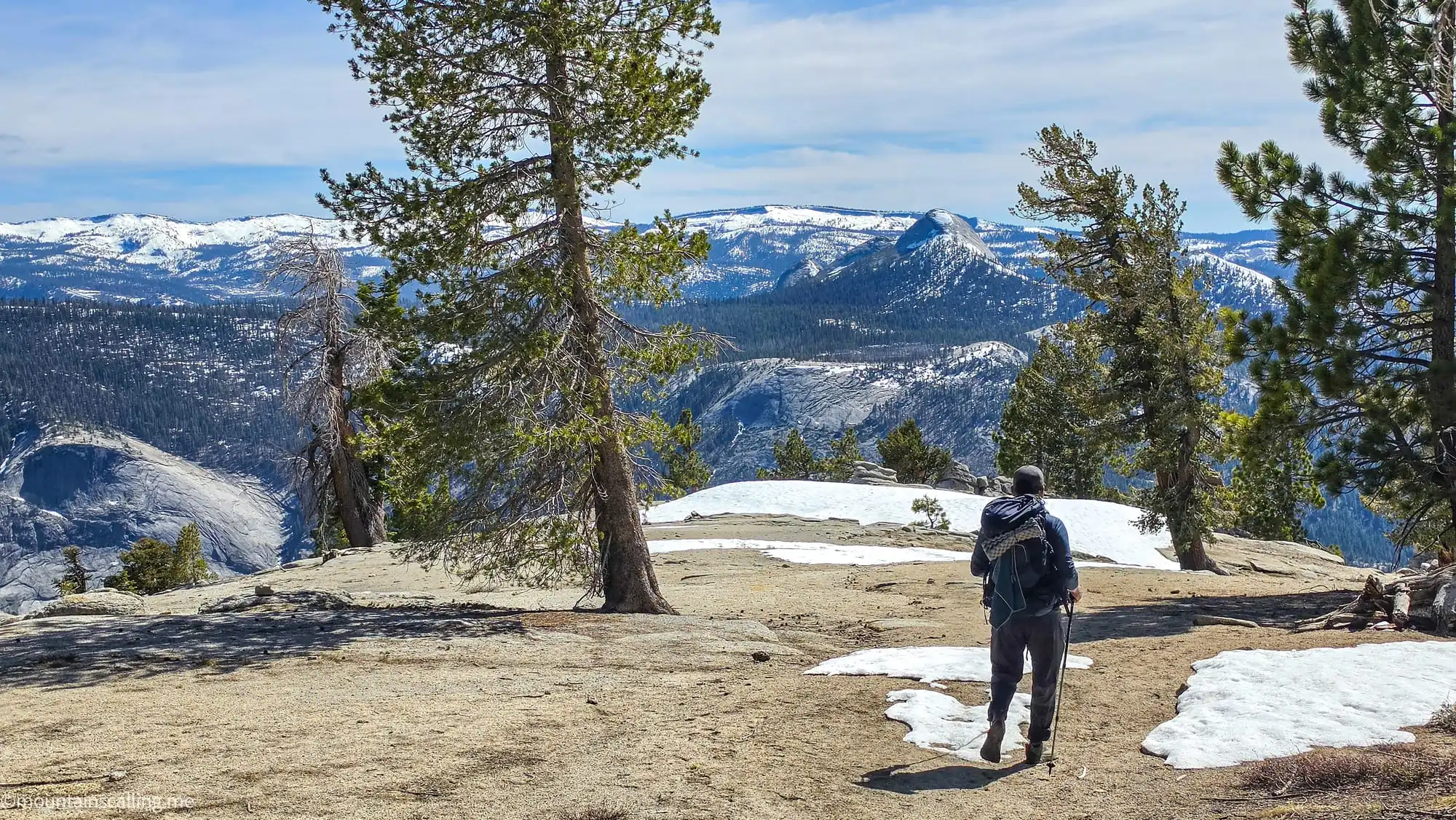 Yosemite Life client hiking across granite slabs with snow patches on Clouds Rest backpacking trail with Yosemite wilderness views
