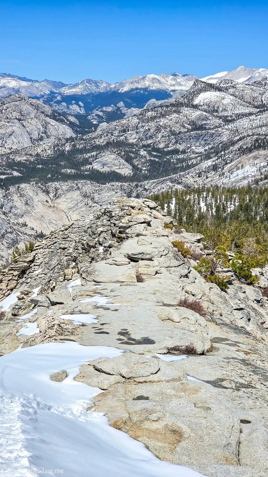 Clouds Rest summit ridge with granite slabs, snow patches, and panoramic mountain views across Yosemite