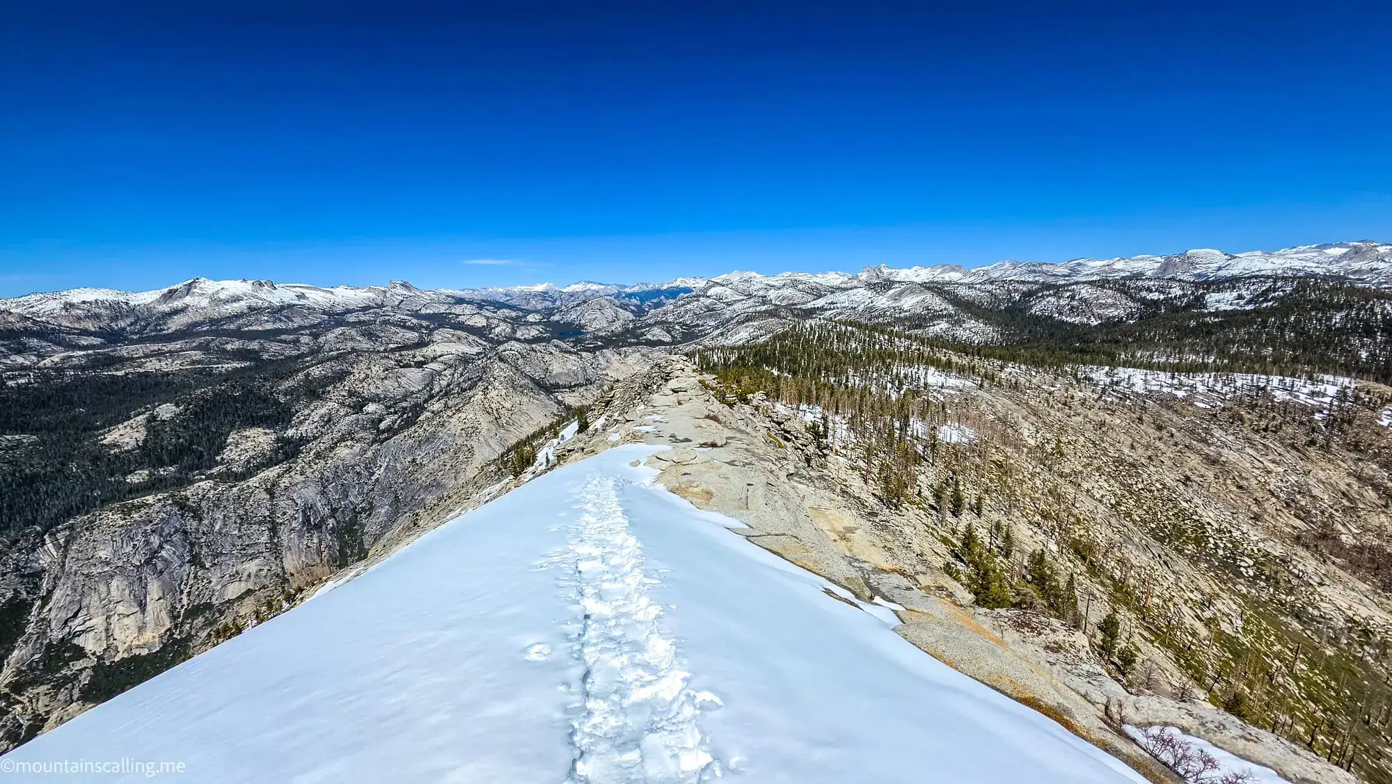 Snow-covered trail on Clouds Rest summit with panoramic Sierra Nevada mountain views in Yosemite wilderness