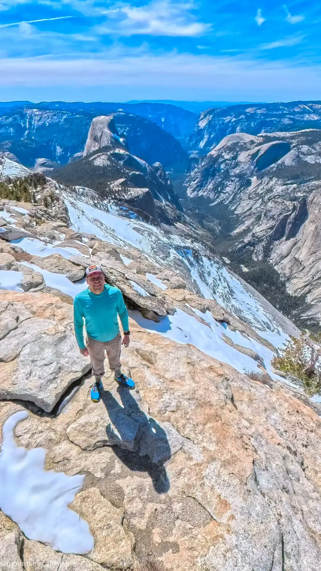 Eric Kufrin on snowy granite summit with Half Dome and Yosemite Valley panorama behind him on Clouds Rest hike