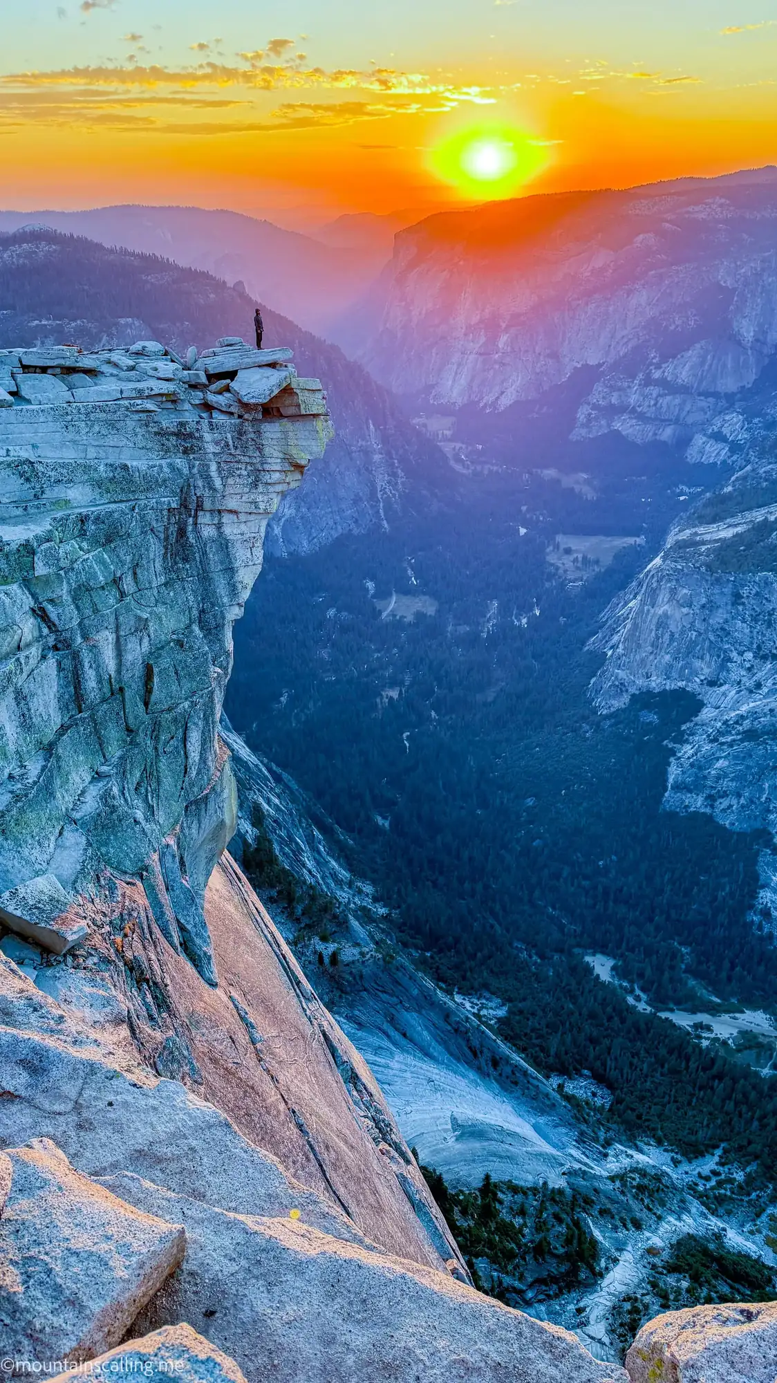 Hiker silhouetted on Half Dome summit cliff edge at sunset overlooking Yosemite Valley granite formations
