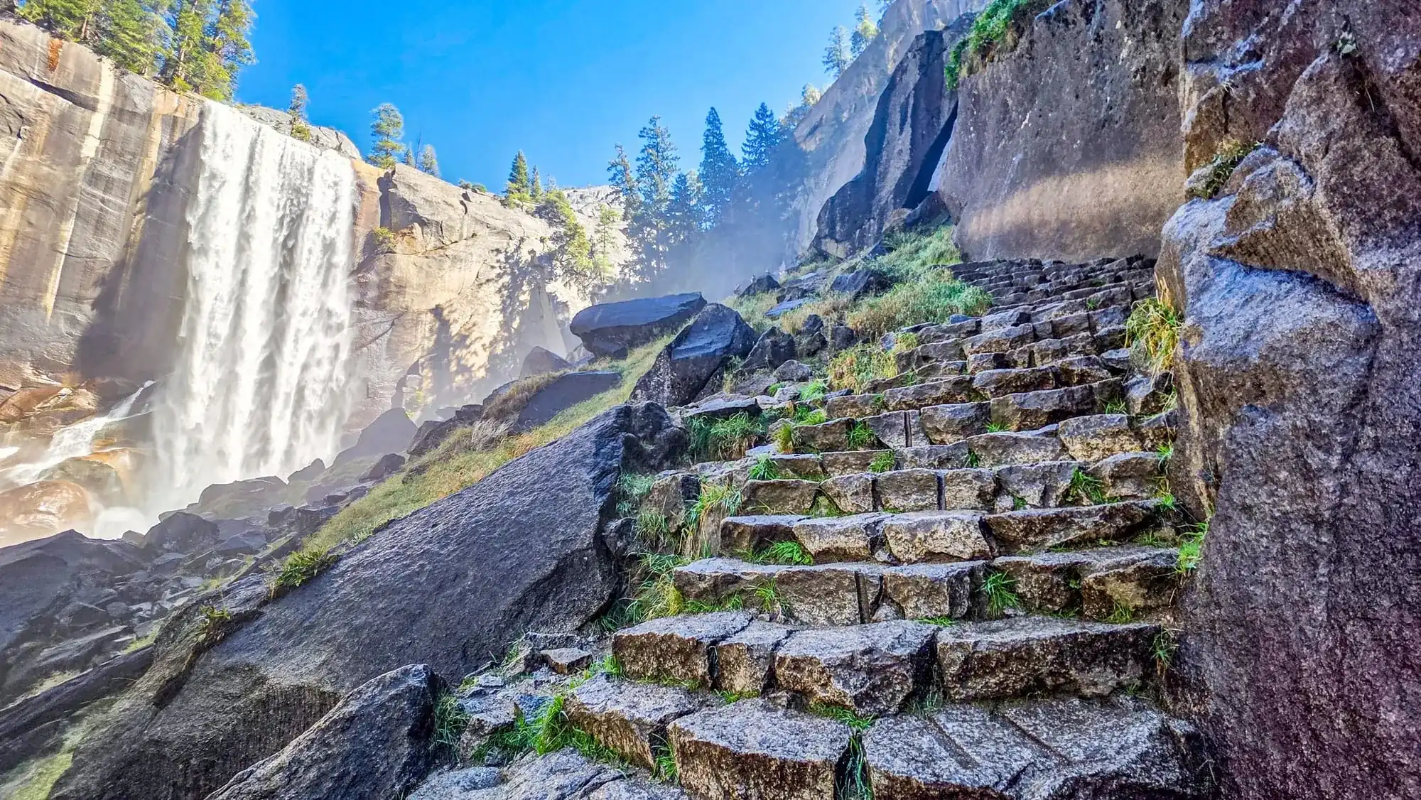 Stone steps of the Mist Trail climbing beside Vernal Fall with mist spray and granite cliffs in Yosemite