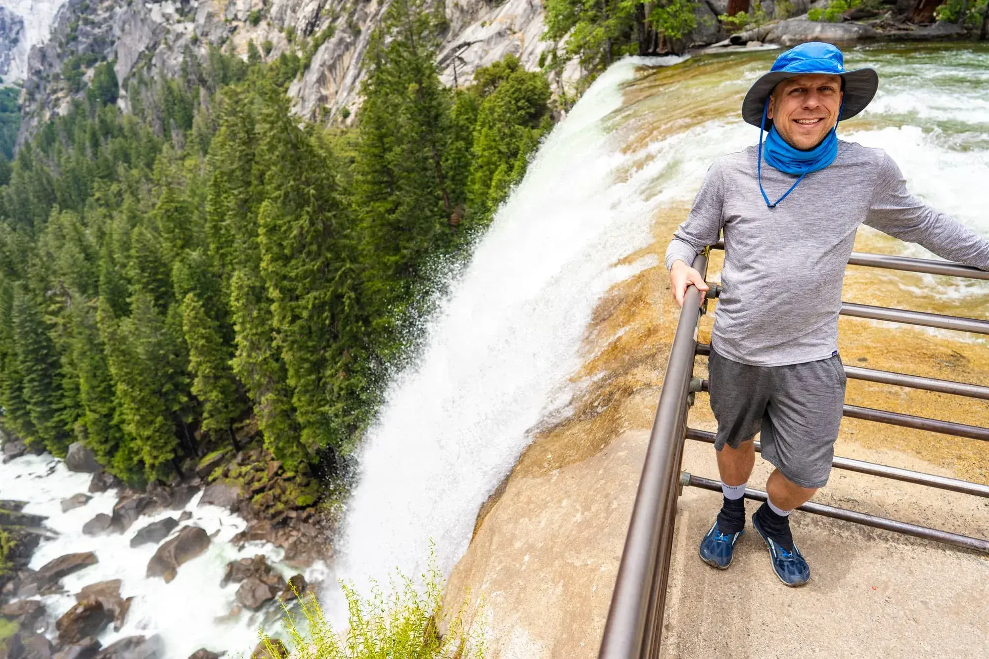 Hiker at Vernal Fall brink on Mist Trail with waterfall cascading into granite gorge and forest below