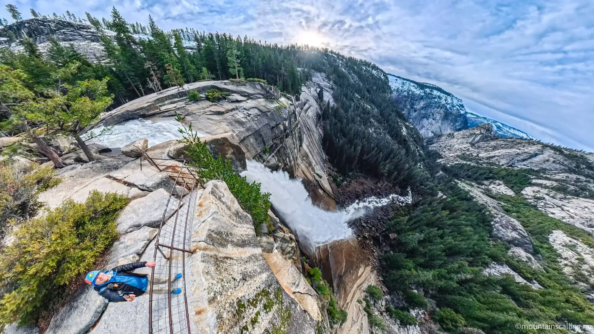 Hiker at Nevada Fall brink on Mist Trail with safety railings and 594-foot drop into Merced River canyon