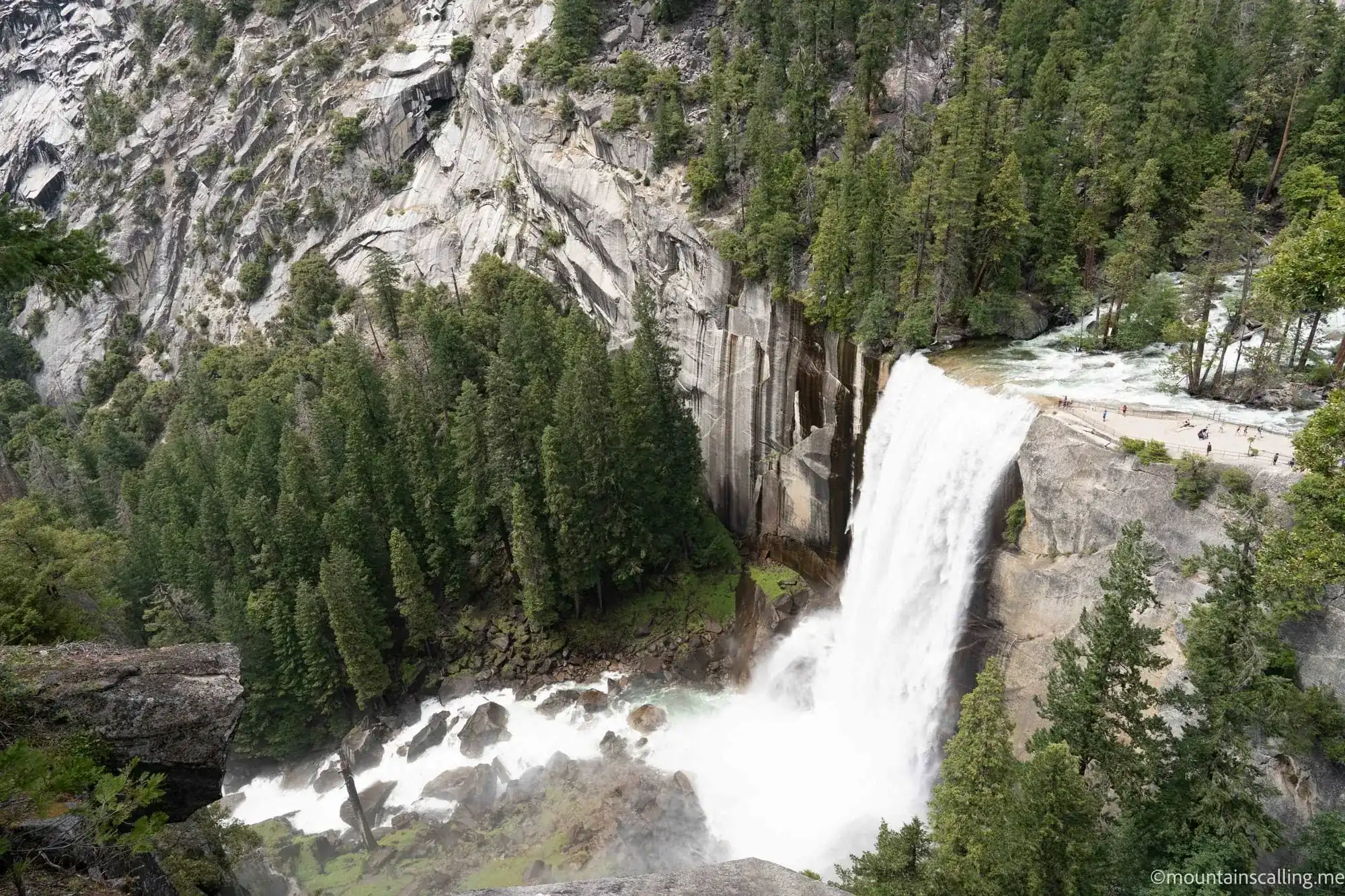 Vernal Fall cascading down granite cliff on Mist Trail with hikers visible at base showing massive scale
