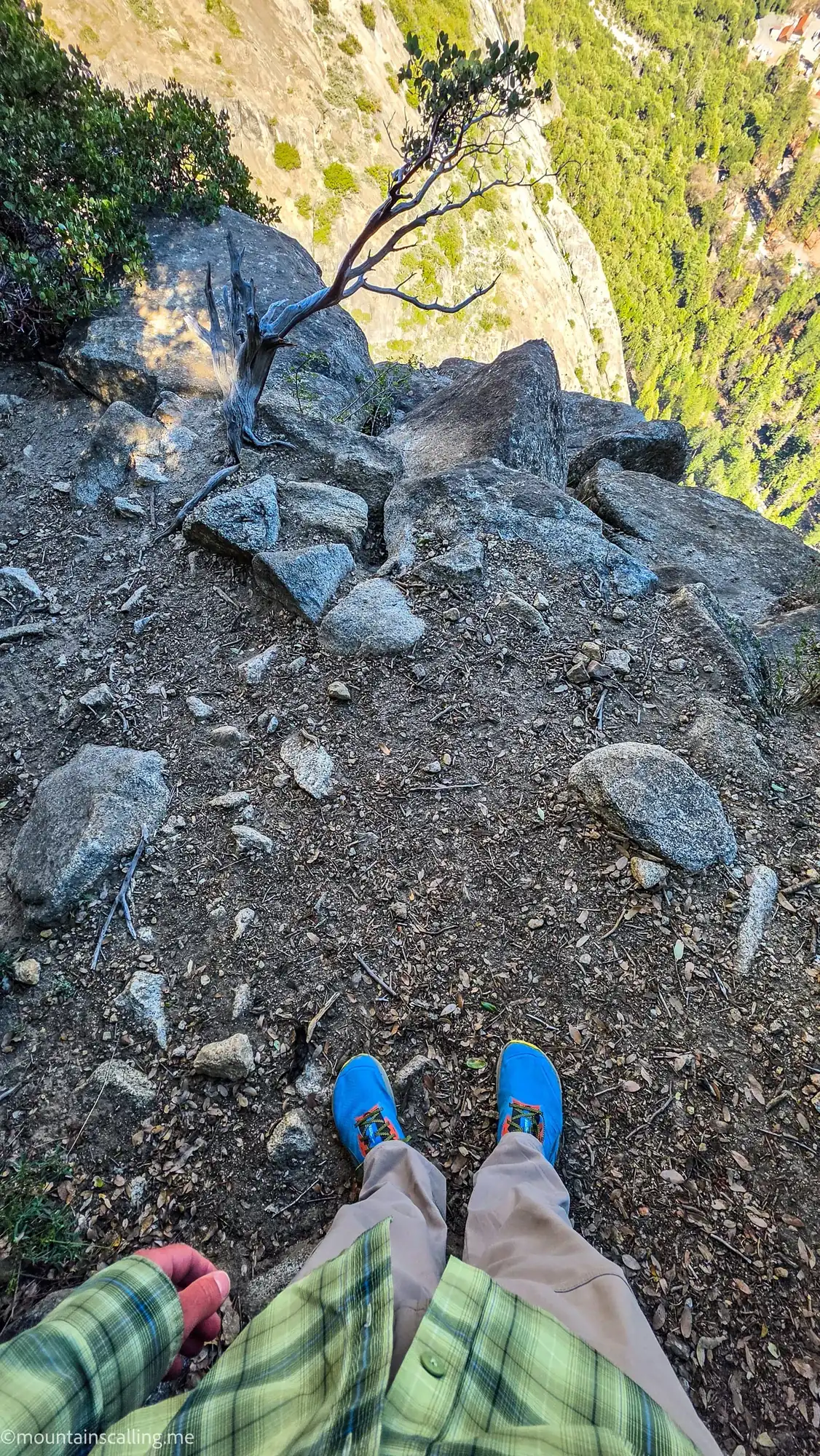 Hiker's perspective from rocky ledge at OMG Point overlooking Yosemite Valley with blue shoes visible