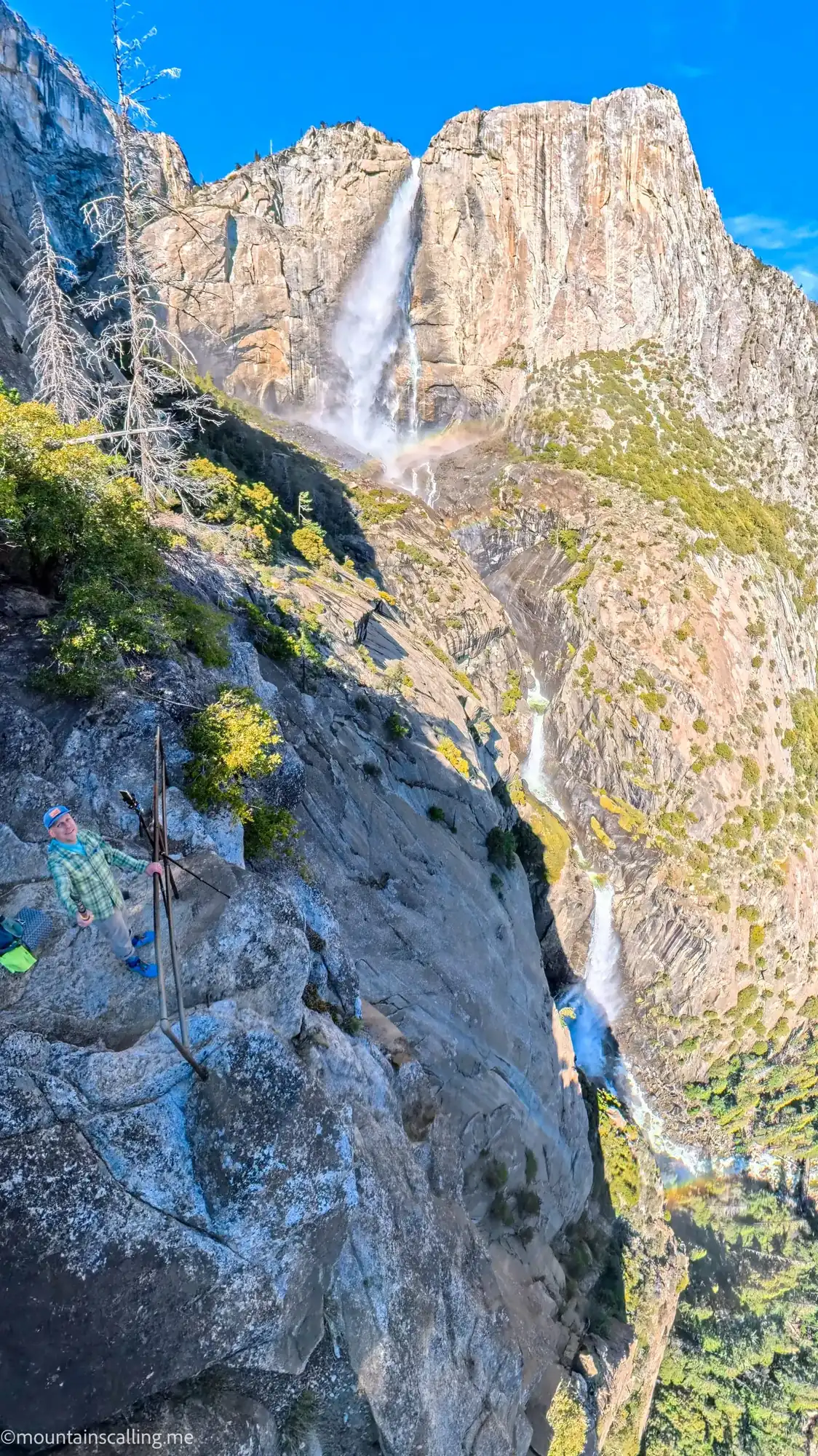 Hiker on rocky outcrop capturing Yosemite Falls with rainbow in mist from OMG Point viewpoint