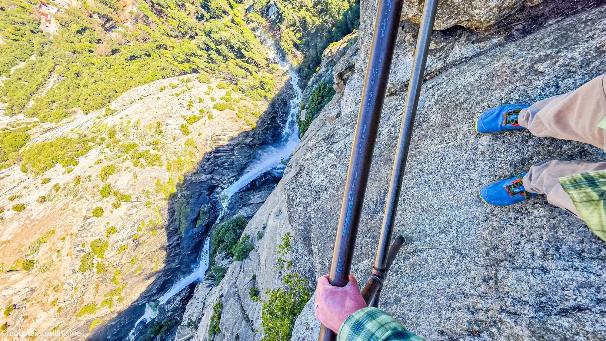 Hiker holding metal railing at OMG Point overlooking Yosemite Valley waterfall and granite cliffs below