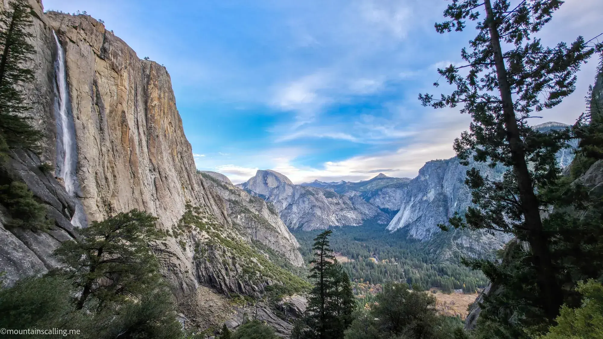 Upper Yosemite Falls cascading down granite cliff with Half Dome and Yosemite Valley visible from Falls Trail viewpoint