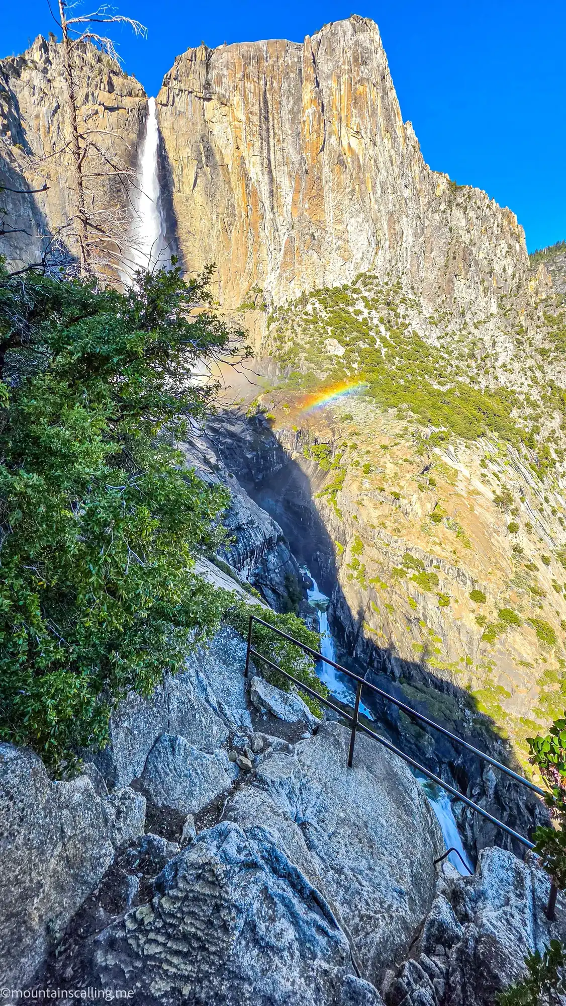 Yosemite Falls with rainbow in mist viewed from OMG Point stone steps with handrail, granite cliffs above