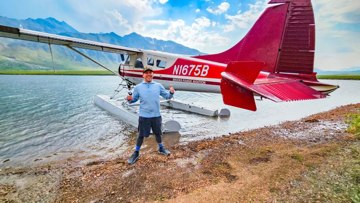 Eric Kufrin giving thumbs up next to floatplane on remote Gates of the Arctic lake with mountains in background