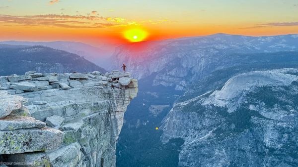 Hiker standing on Half Dome summit cliff edge at sunset overlooking Yosemite Valley granite peaks