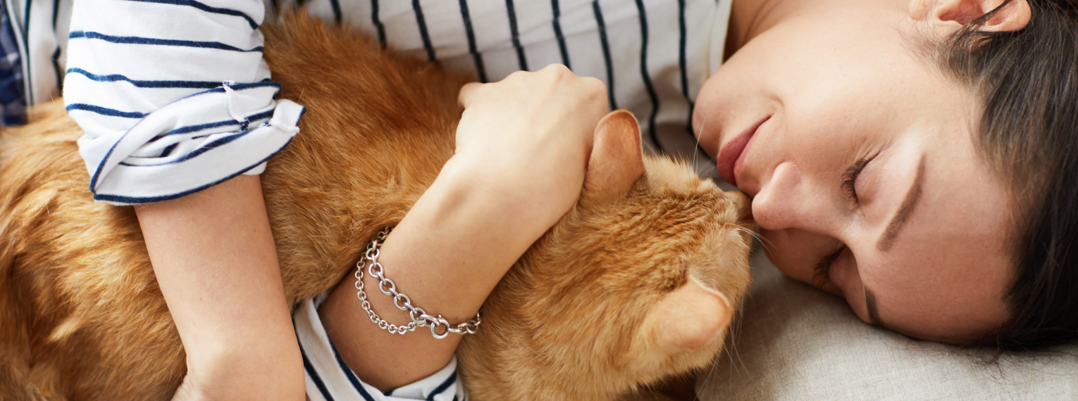 Eine Frau schmust im Liegen mit einer Katze.