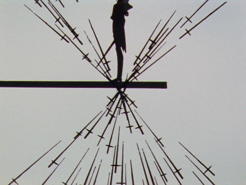 a man stands on a bridge. swords from above and below crash at a point beneath his feet.