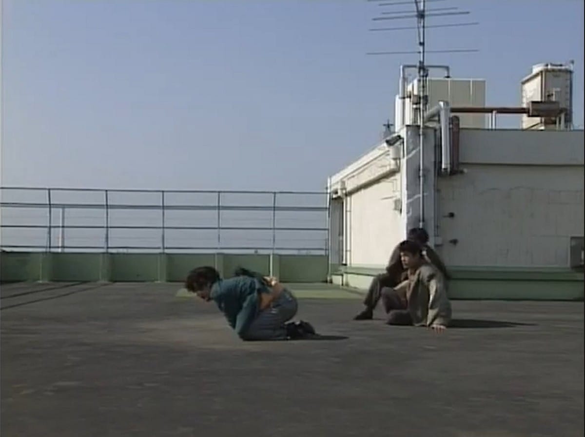 hamura and shinjyo, who are sitting on the school roof, stare at the english teacher fujimura, who is kneeling on the ground