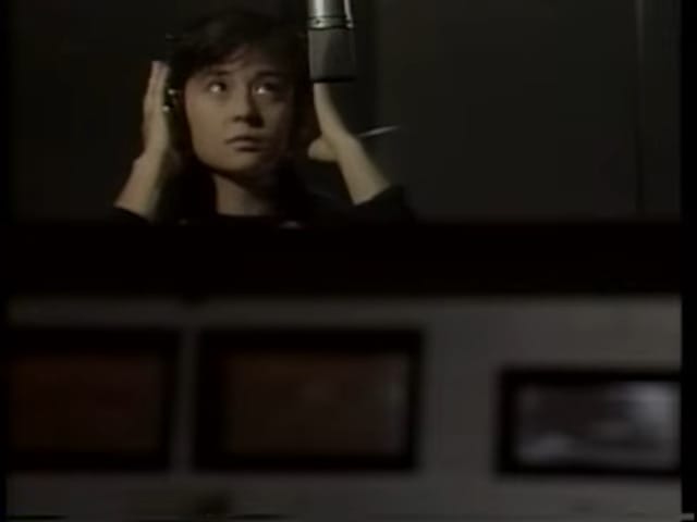 a young woman holds her hands to her headphones in the recording booth.