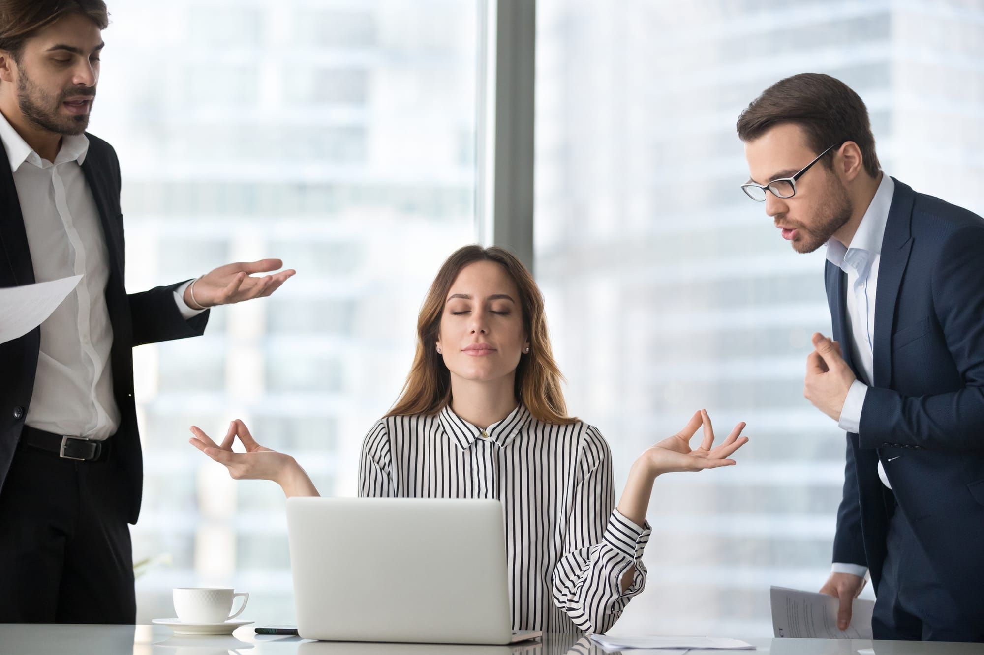 Calm female worker meditate at workplace managing stress not paying attention to angry colleagues