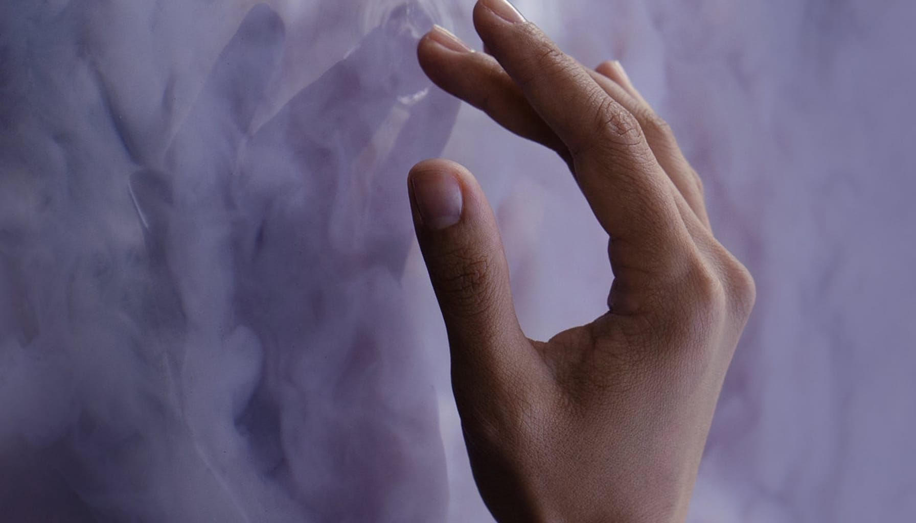 Close-up image of a hand touching a cloudy purple surface