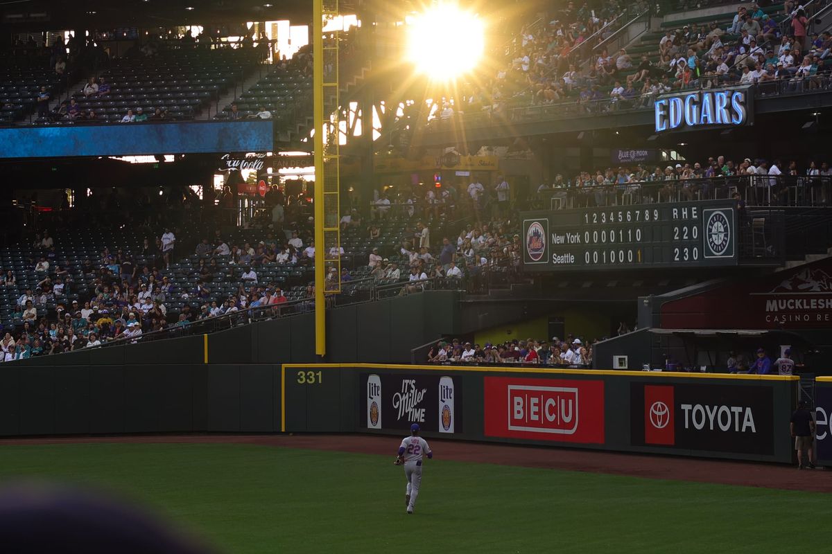 Mets outfielder Juan Soto jogs toward the warning track in left field at T-Mobile Park with the sun shining brightly through the stands above him.
