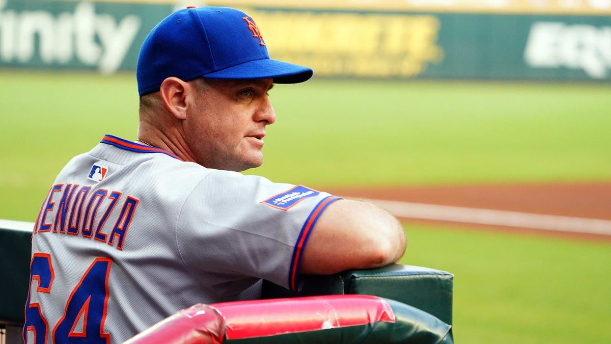 Carlos Mendoza in his Mets uniform, looking out over the playing field from the dugout.